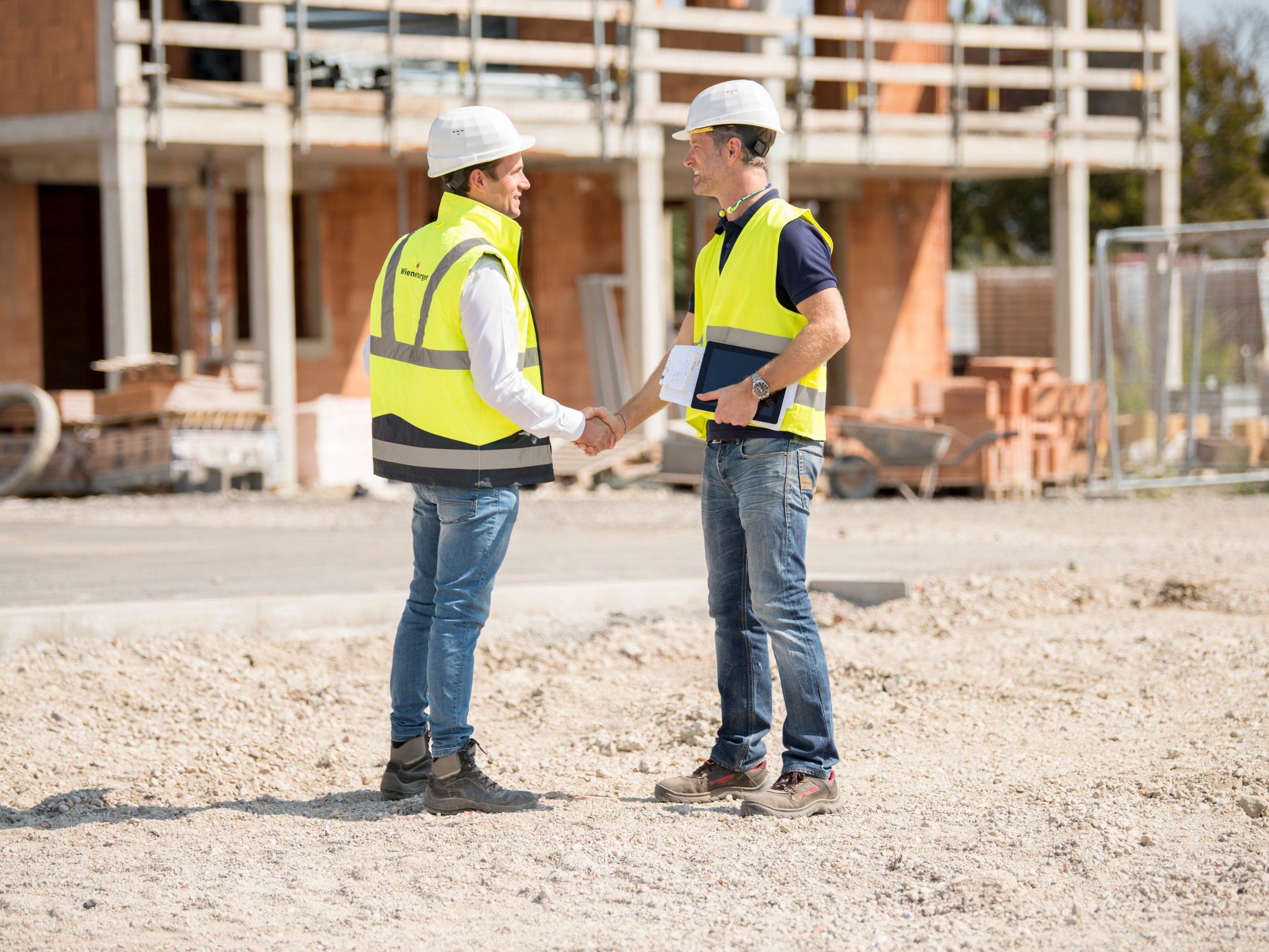 Manager and builder shaking hands on construction site in front of building shell