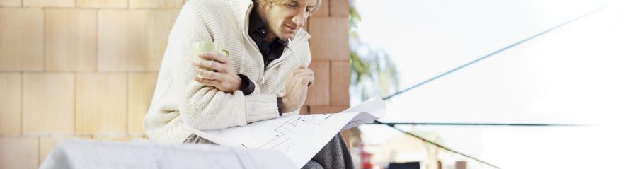 Man with blueprint in unfinished building thinking