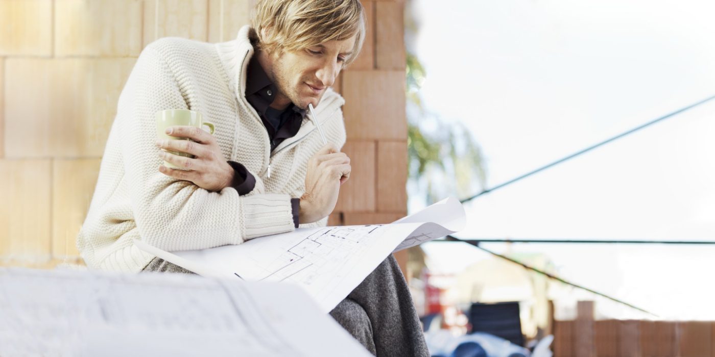 Man with blueprint in unfinished building thinking