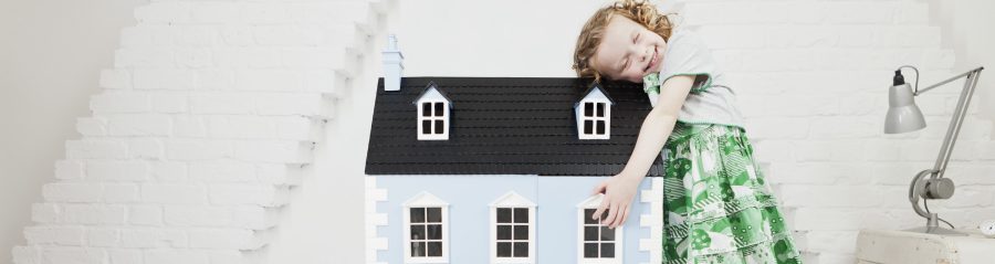 Happy girl leaning against doll house in attic loft