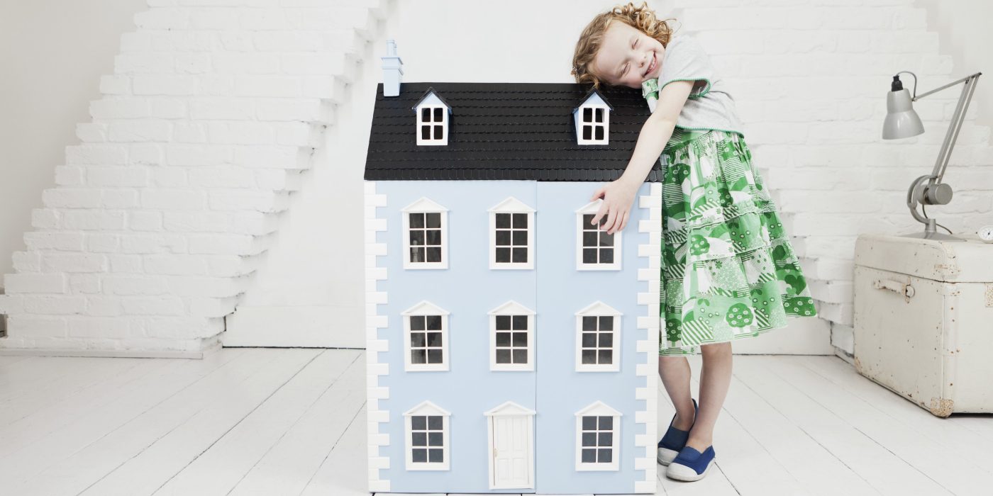 Happy girl leaning against doll house in attic loft