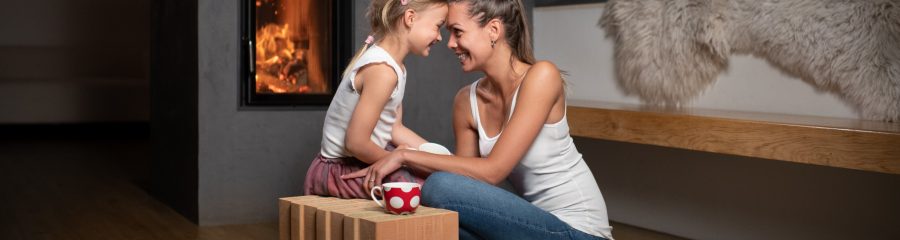 Žena maminka sedící s dítětem u teplého krbu v popředí cihla Porotherm T Profi
