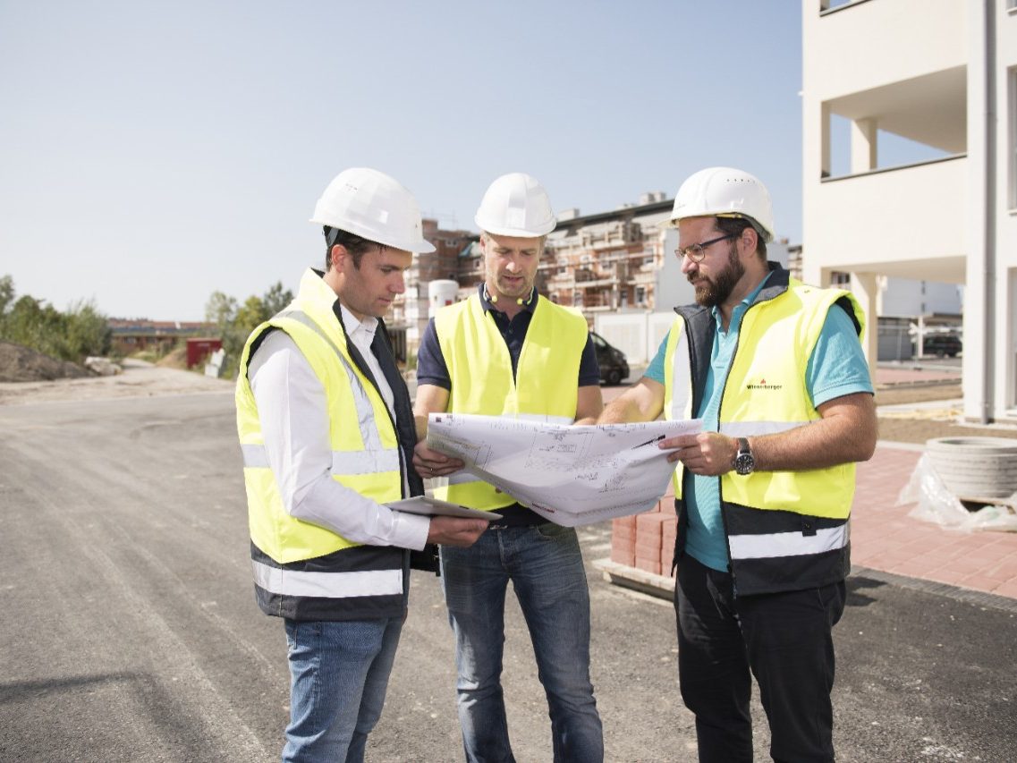 Three building professionals on a construction site studying a blueprint