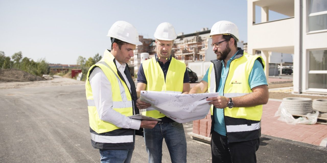 Three building professionals on a construction site studying a blueprint