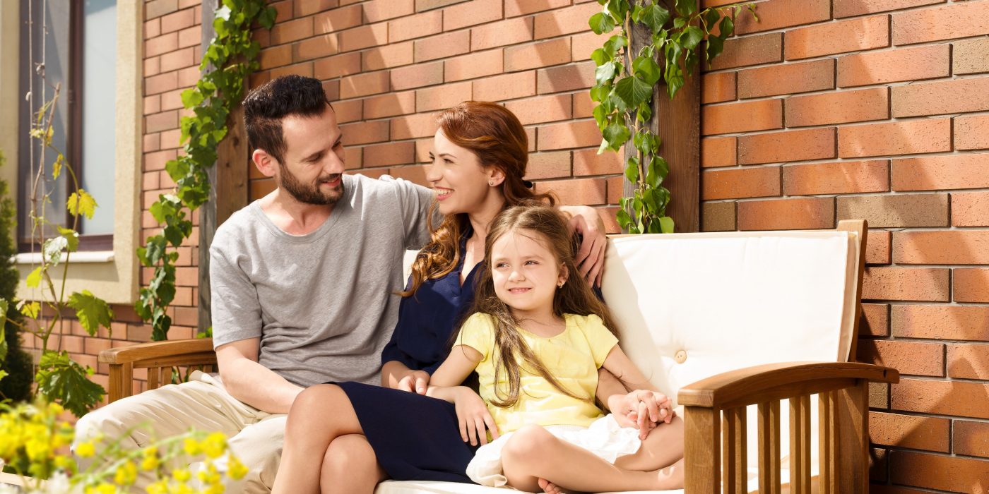 Young family sitting on garden bench in front of brick-lined façade