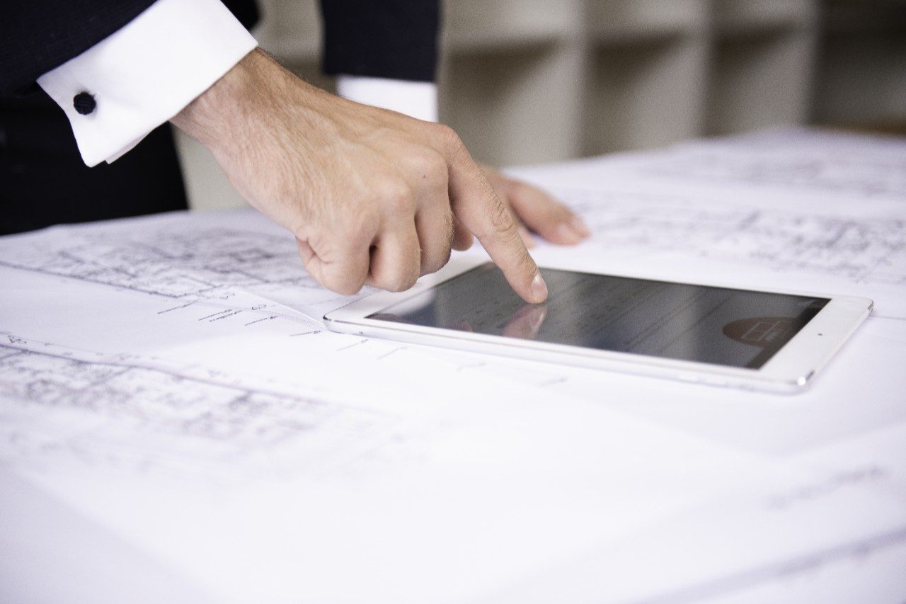 Hand typing on tablet computer lying on blueprint