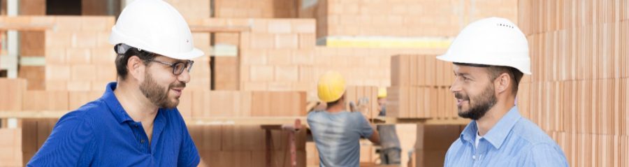 Building professionals talking at construction site next to foil wrapped pallette of brick blocks. > There is another version of this image available without the worker in the background - WB002389