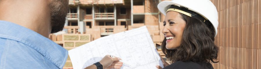 Female architect with hard hat and blueprint-casing inside a building shell touching a brick