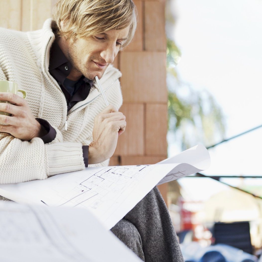 Man with blueprint in unfinished building thinking