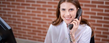 Smiling woman sitting next to computer screen holding a telephone receiver