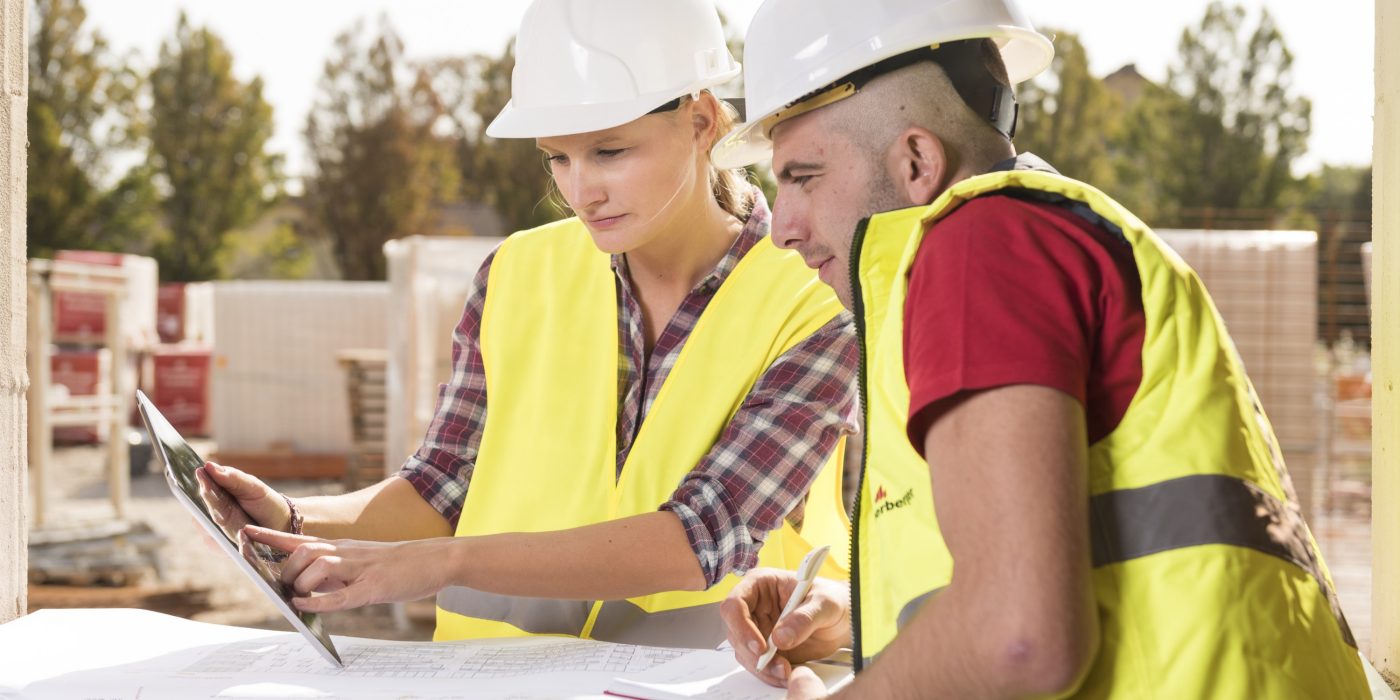 Woman pointing at tablet with male coworker taking notes at construction site, Fast Forward Commercial Excellence