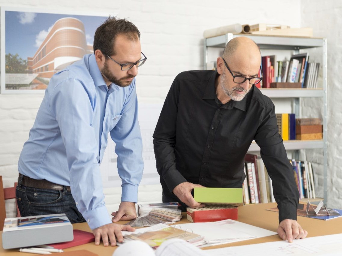 Wienerberger project manager and architect with glazed facing bricks looking at blueprint at architect's office
